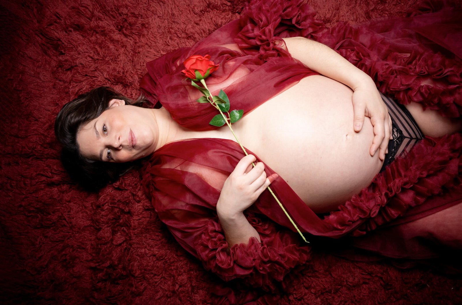 a pregnant woman lying on a red carpet holding a rose