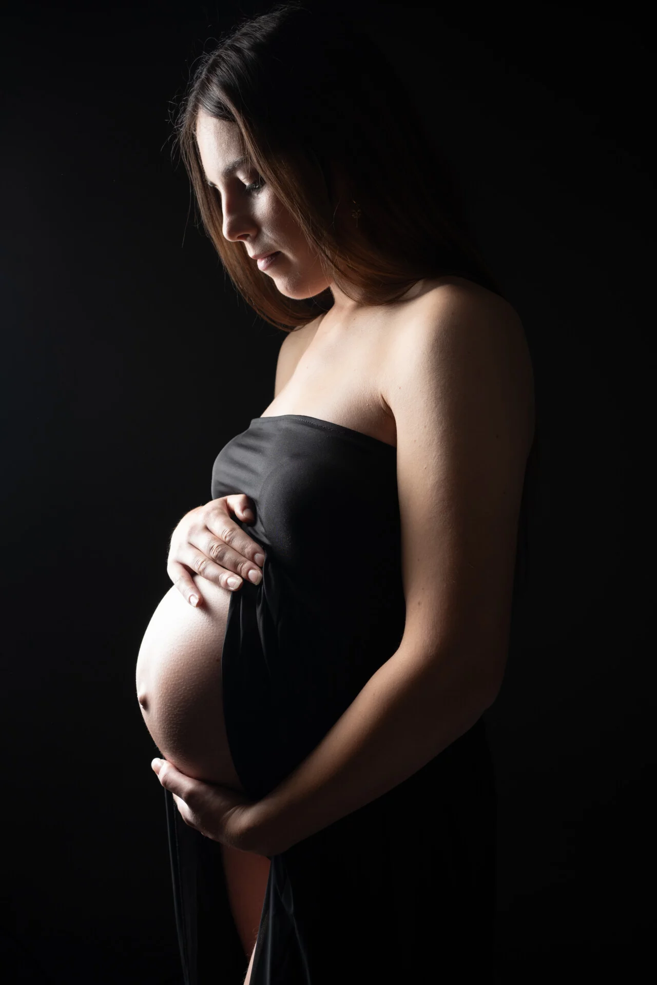 Future maman en robe noire, lumière artistique en contre-jour – séance grossesse en studio près de Rouen
