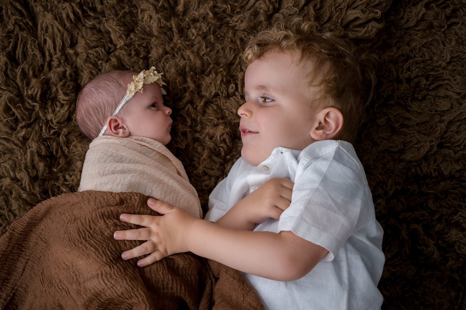 Photo de fratrie réalisée par Yohann Boulanger, photographe de famille en Normandie, bébé emmailloté et grand frère complices