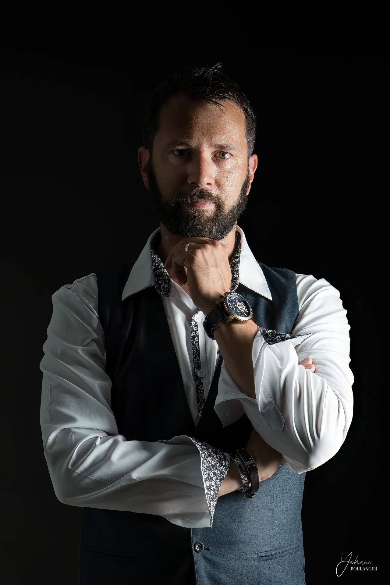 Portrait studio d’un homme barbu en chemise blanche et gilet, sur fond noir, avec une lumière dramatique