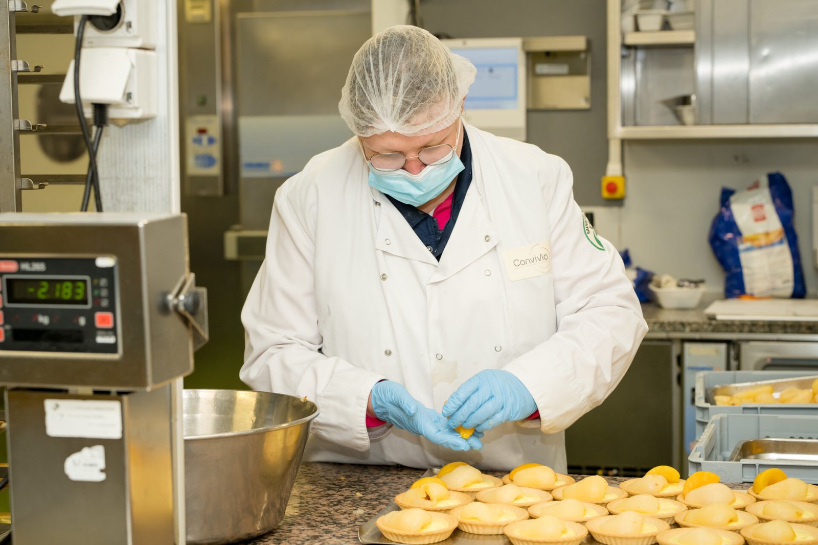 Cuisinière en blouse blanche préparant des tartelettes en cuisine collective CONVIVIO à Bois Himont