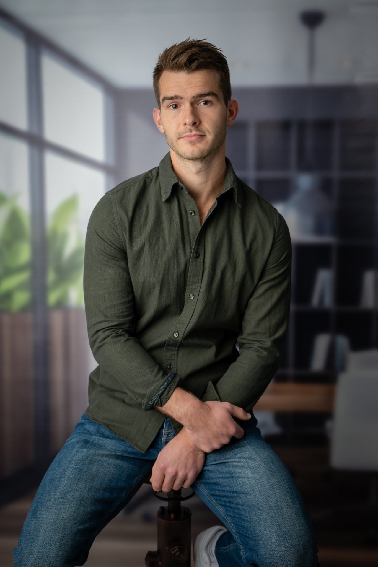 Homme assis dans un environnement professionnel, portant une chemise verte et un jean