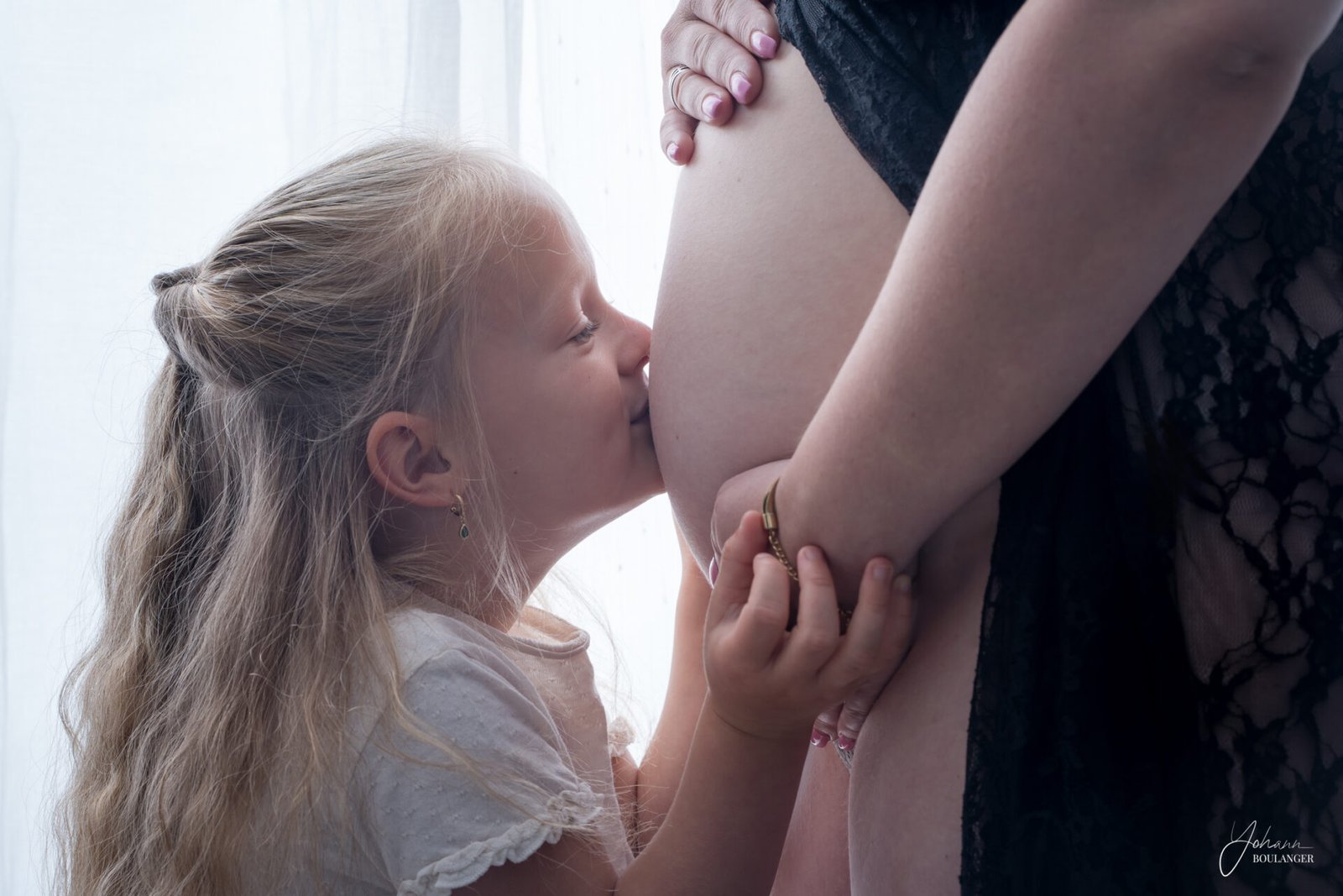 Jeune fille embrassant le ventre rond de sa mère enceinte, moment de tendresse capturé par un photographe professionnel en Normandie.