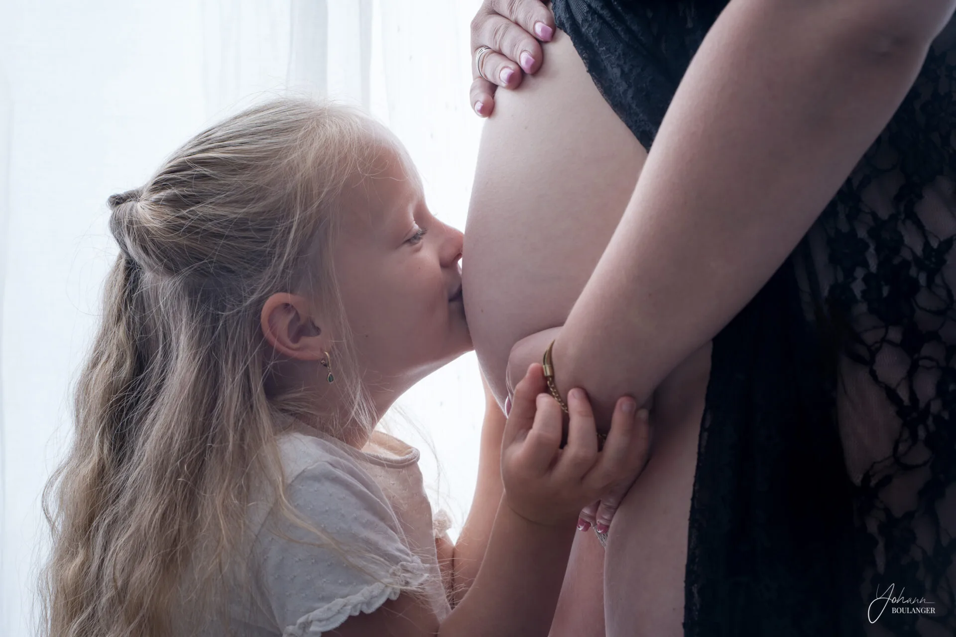Jeune fille embrassant le ventre rond de sa mère enceinte, moment de tendresse capturé par un photographe professionnel en Normandie.