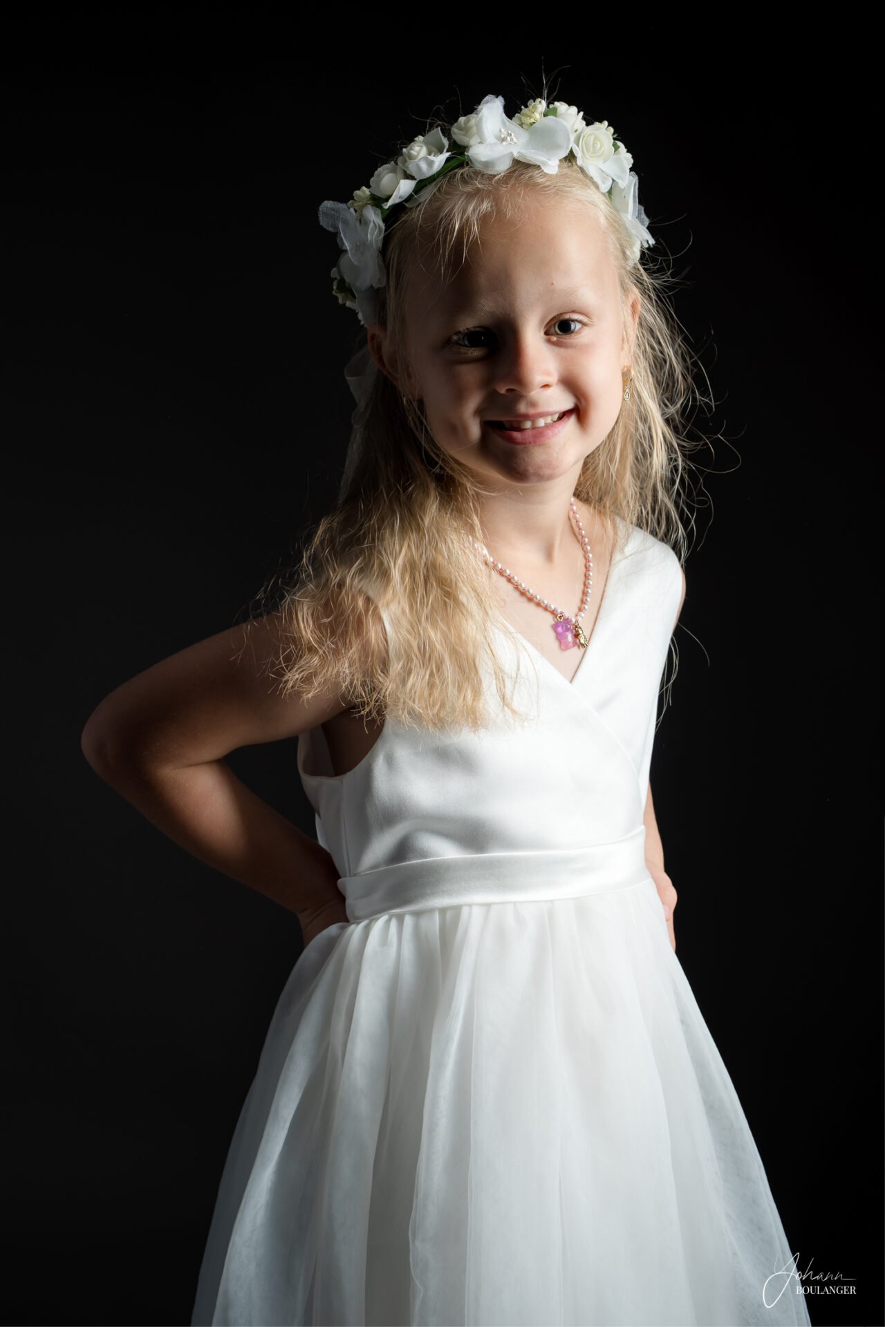 Portrait de fillette souriante en robe blanche et couronne de fleurs, lumière professionnelle en studio