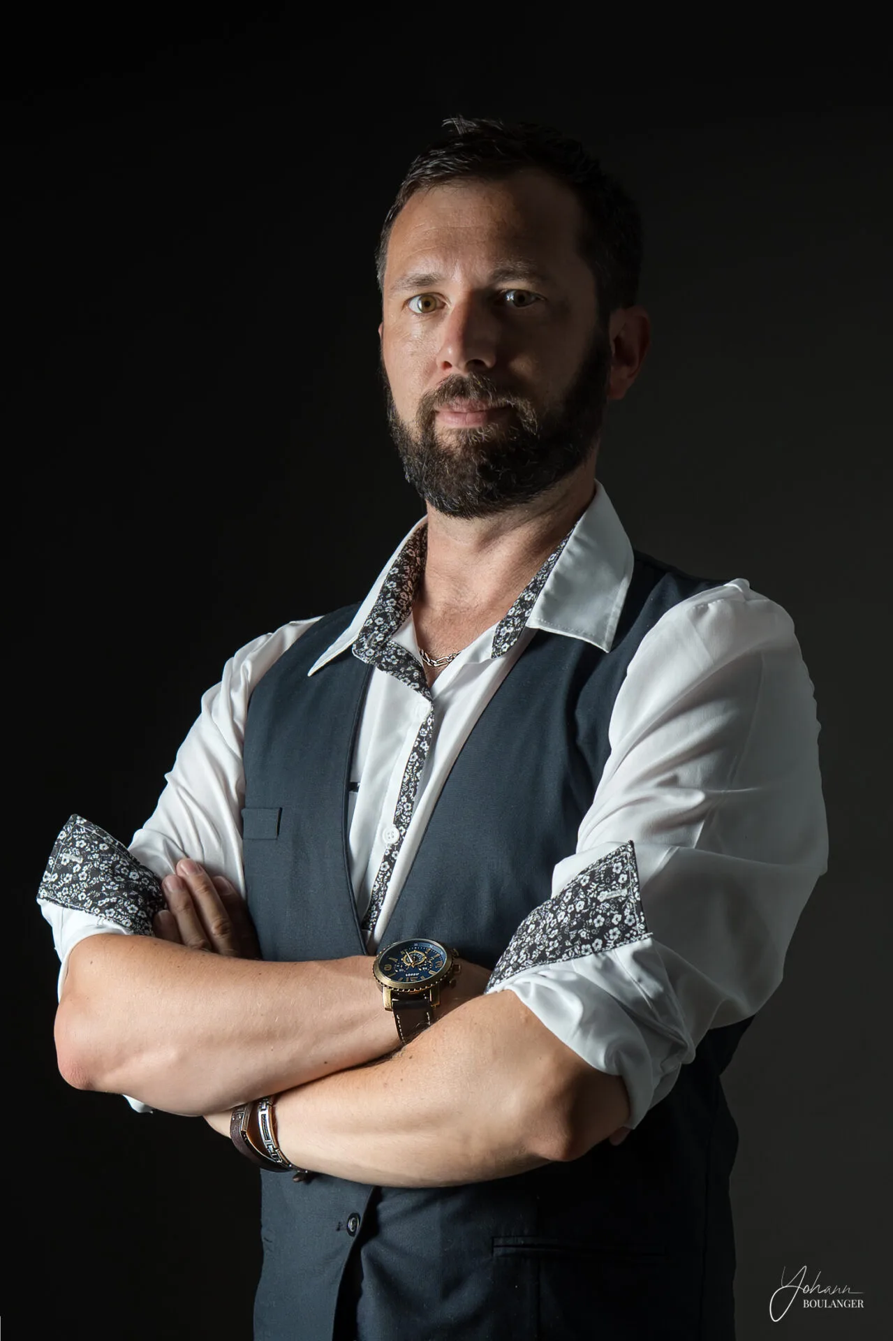 Portrait studio d’un homme barbu en chemise blanche et gilet, sur fond noir, avec une lumière dramatique