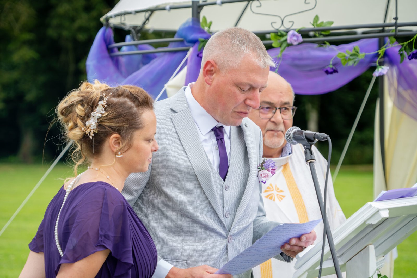 Lecture de vœux de mariage par un couple accompagné d’un officiant, cérémonie laïque en extérieur.