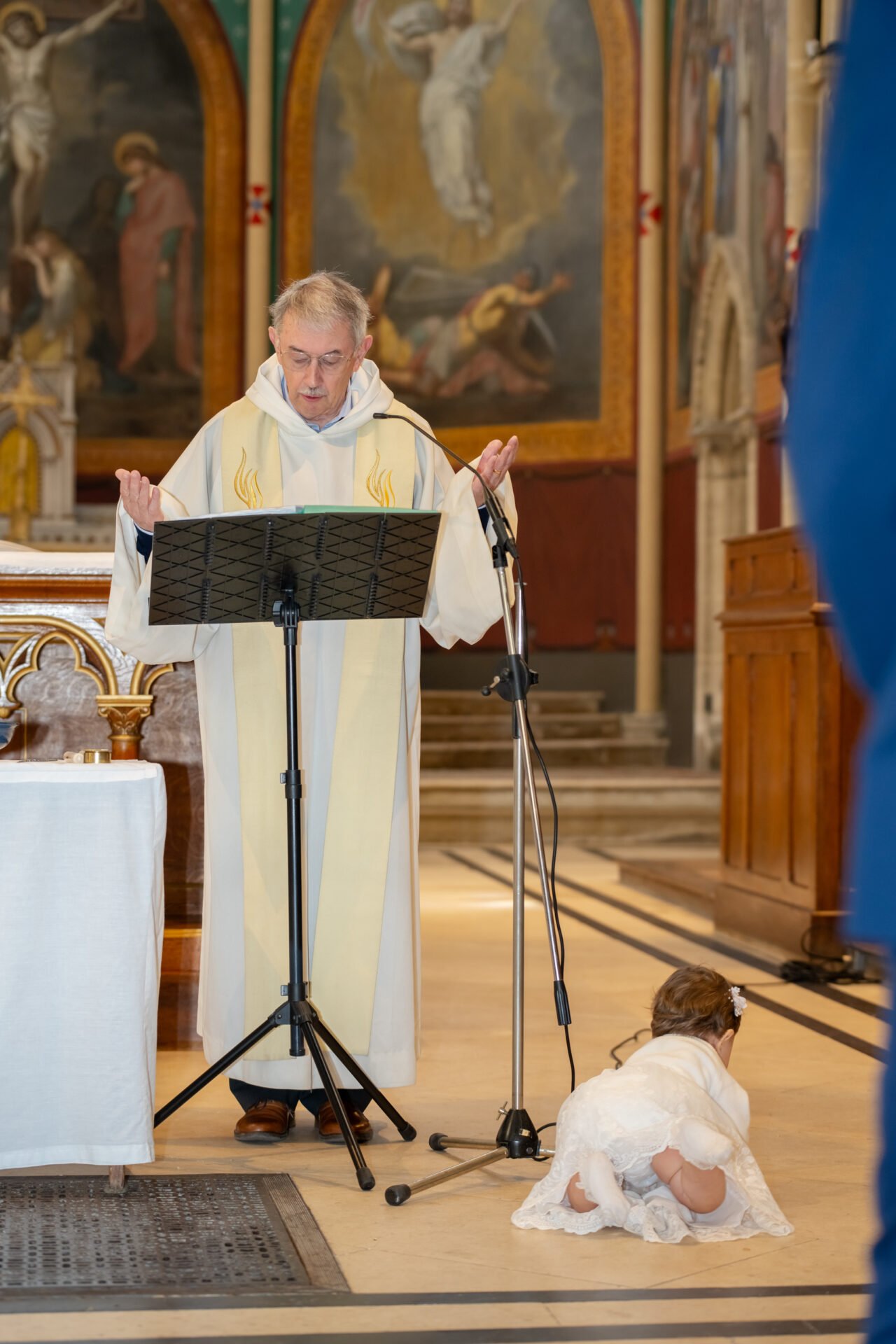 Reportage photo de baptême en Normandie – prêtre en prière et enfant jouant dans l’allée de l’église.